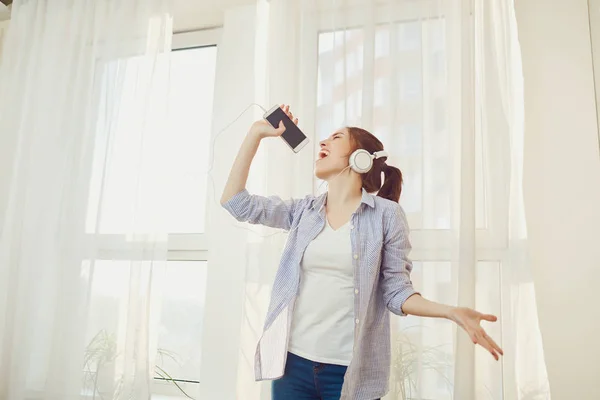 Una chica con auriculares canta una canción contra la ventana  . — Foto de Stock