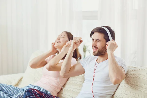 Pareja en auriculares tumbados en el sofá escuchando música en la habitación . — Foto de Stock