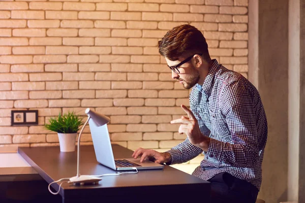 Um homem barbudo freelancer com um laptop trabalha à noite . — Fotografia de Stock