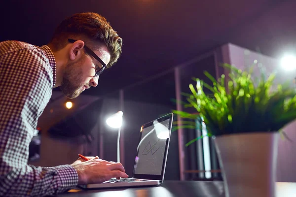 Um homem barbudo freelancer com um laptop trabalha à noite . — Fotografia de Stock