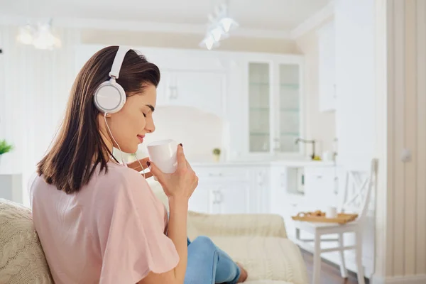 La chica en los auriculares yace en el sofá, escuchando música — Foto de Stock