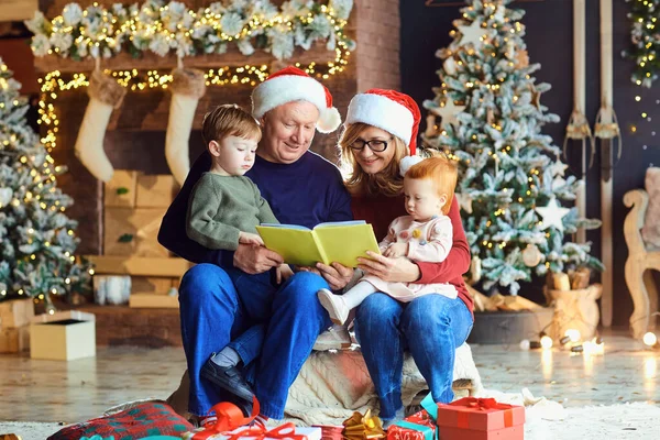 Grootouders lezen een boek voor kinderen in Kerstmis — Stockfoto