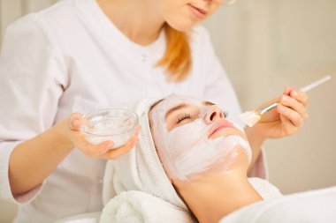 Bir kozmetolojist bir kadına maske uygular..