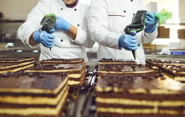 Los confiteros adornan la crema de la bolsa sobre la torta de chocolate en la panadería . — Foto de Stock