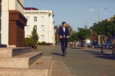 Kasklı genç adam yazın bir şehir caddesinde elektrikli scooter kullanıyor.
