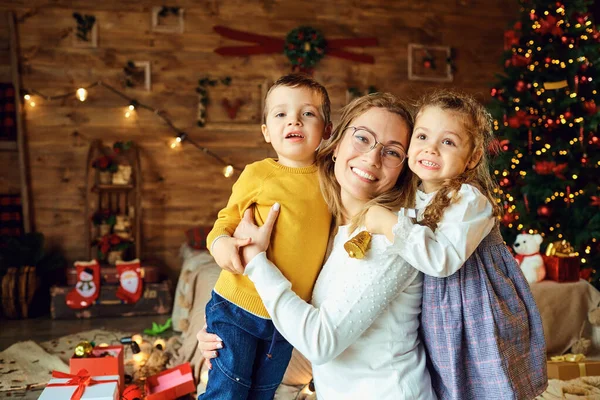 Счастливая мама обнимает детей в комнате на Рождество — стоковое фото