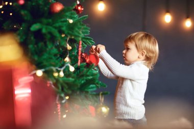 Küçük bir çocuk Noel ağacını süslüyor.