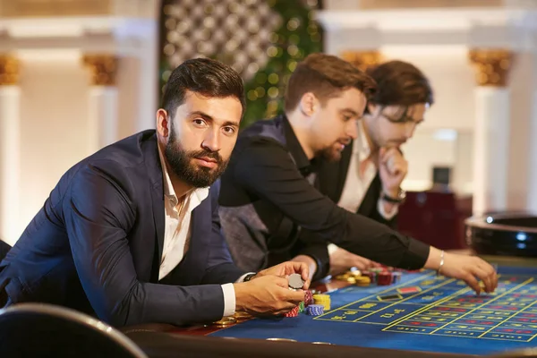 En man i kostym med ett glas whisky sitter på bordet Roulette spela poker på ett kasino. — Stockfoto