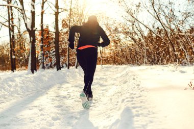 Bir kız kışın gün batımında parkta koşar.