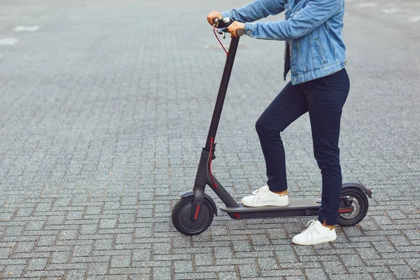 Joven en un casco monta un scooter eléctrico en una calle de la ciudad en verano — Foto de Stock