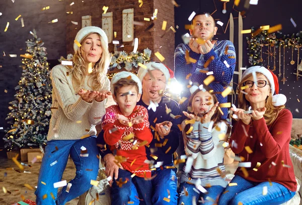 Grande famille heureuse soufflant des confettis à la maison pour Noël . — Photo