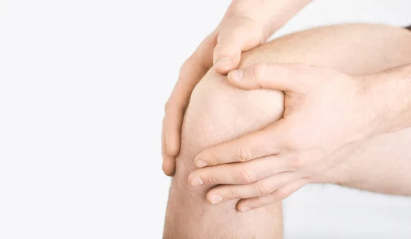 Ein Mann in Unterwäsche hält sein Knie mit einer Hand auf einem grauen Hintergrund. — Stockfoto