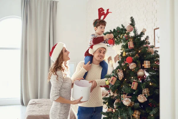 Familia en suéteres pintan el árbol de Navidad en la casa . — Foto de Stock