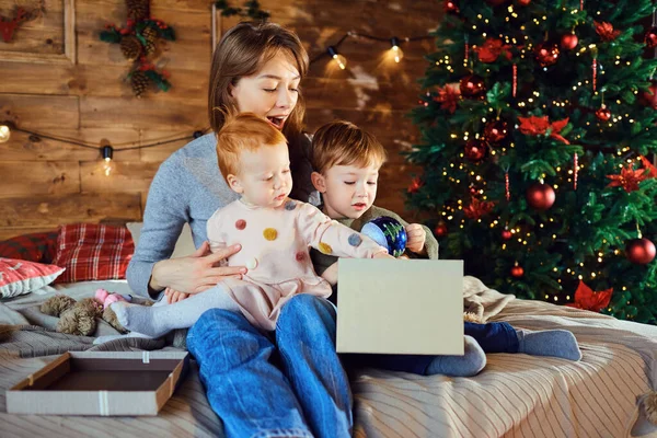 Moeder met kinderen kijken giftson het bed in Kerstmis. — Stockfoto