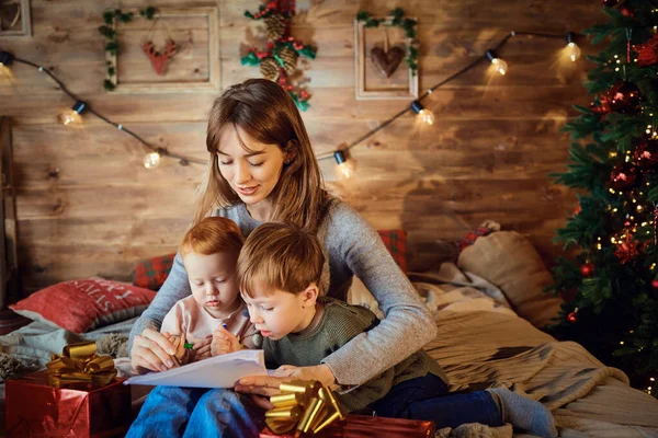 Mutter mit Kindern schaut Weihnachtsgeschenken im Bett zu. — Stockfoto