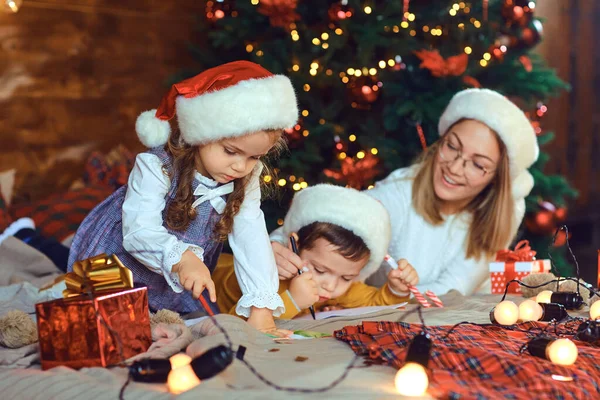 Mom with children draws in the room with the Christmas tree. Stock Photo