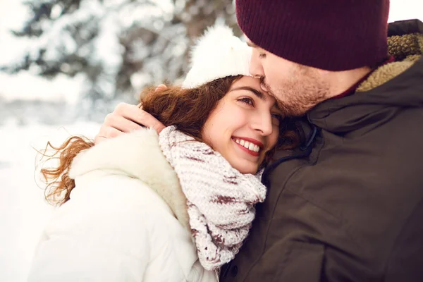 Facet całuje uśmiechniętą dziewczynę zimą w śniegu. — Zdjęcie stockowe