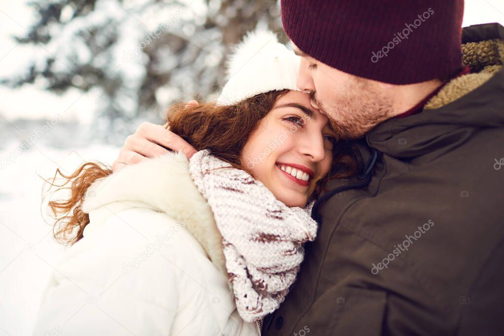 The guy kisses a smiling girl in the winter in the snow