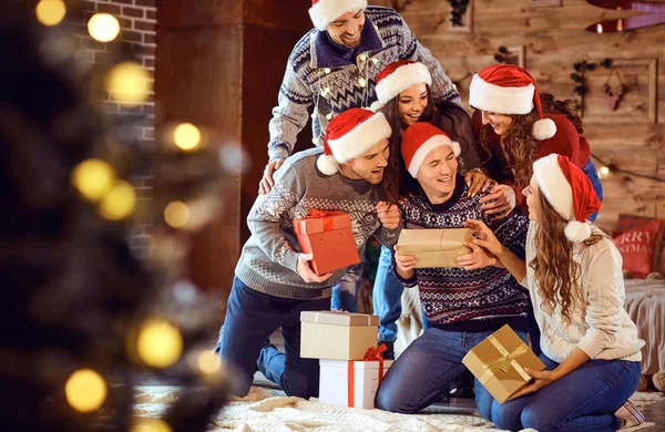 Przyjaciele w kapeluszach Mikołajów zmieniają prezenty na przyjęciu świątecznym — Zdjęcie stockowe