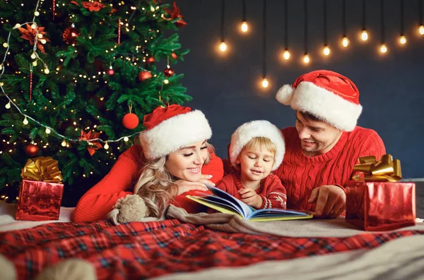 Familie mit Kind Ich lese zu Hause ein Buch mit einem Weihnachtsbaum. — Stockfoto