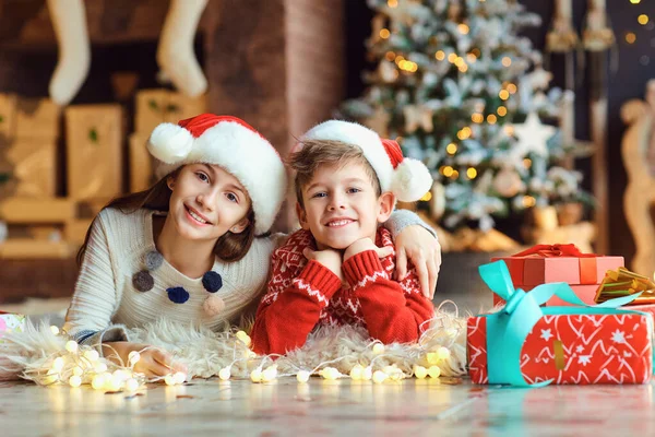 Kinderen liggen op de grond in Santas hoeden op Kerstmis. — Stockfoto