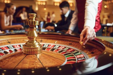 Hand of a croupier with a ball on a roulette wheel during a game in a casino. clipart
