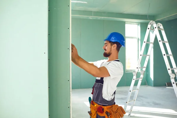 Рабочий строитель устанавливает гипсокартонную гипсокартонную стену на стройке — стоковое фото