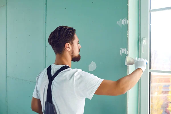 Trabalhador construtor de gesso rebocando uma parede de drywall em um canteiro de obras dentro de casa — Fotografia de Stock