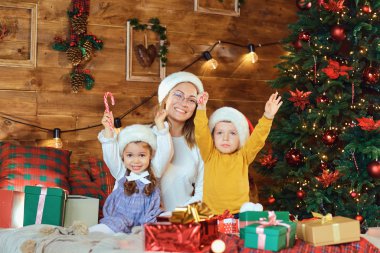 Anne ve çocuklar Noel hediyelerinin arasında oturuyorlar.