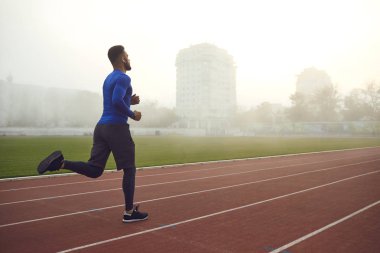 Genç bir atlet siste bir stadyumda koşuyor..