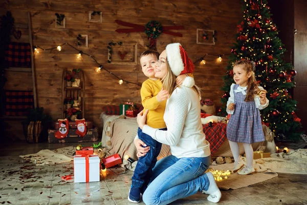 Gelukkig moeder knuffelt kinderen in een kamer met Kerstmis — Stockfoto