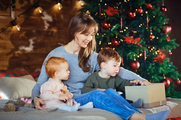 Moeder met kinderen kijken giftson het bed in Kerstmis. — Stockfoto