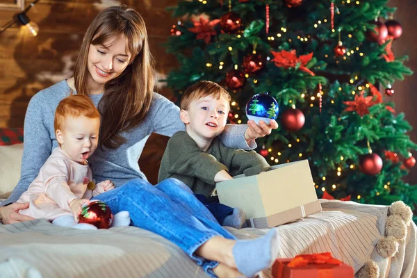 Moeder met kinderen kijken giftson het bed in Kerstmis. — Stockfoto