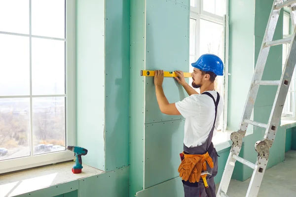 En byggare som står på en stege installerar gipsvägg på en byggarbetsplats — Stockfoto