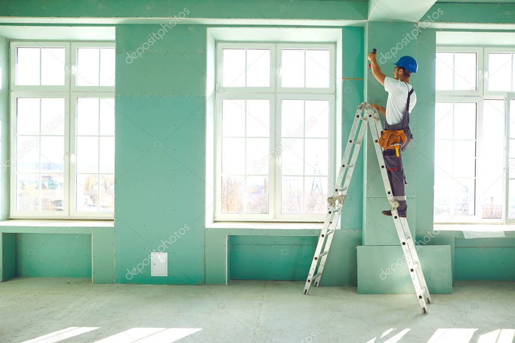 Worker builder installs plasterboard drywall at a construction