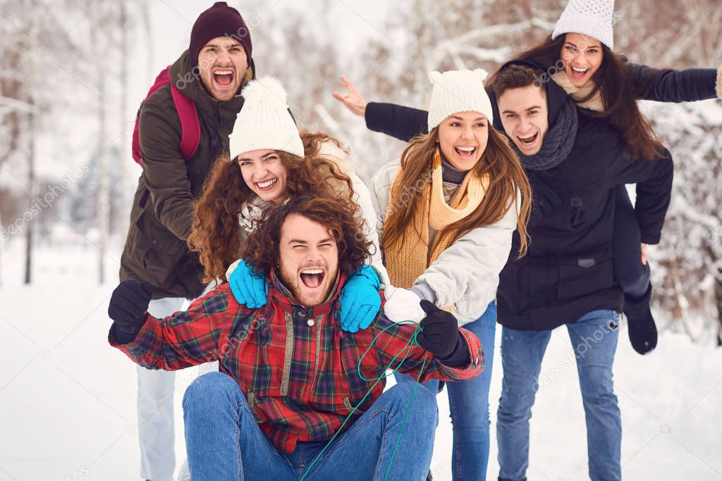 Group of young people enjoying a sled in the snow in winter