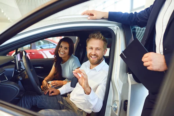 Um casal feliz comprou um carro novo em um showroom do carro . — Fotografia de Stock