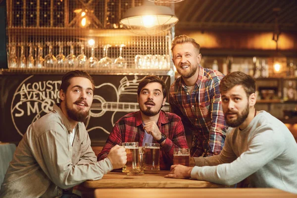 A group of guys watching sports on tv in a pub bar.