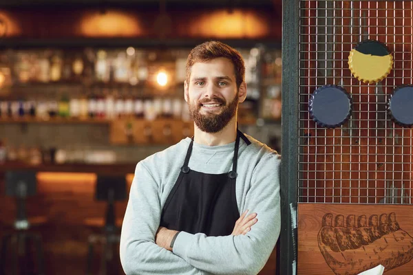 Bärtiger lächelnder Barkeeper-Kellner, der auf dem Hintergrund einer Bar steht. — Stockfoto