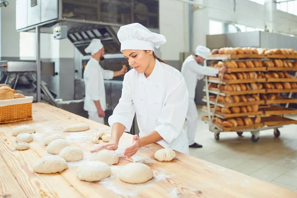 Una mujer panadero sonríe con sus colegas en una panadería . —  Fotos de Stock