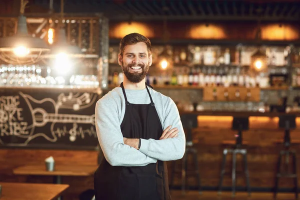 Bärtiger lächelnder Barkeeper-Kellner, der auf dem Hintergrund einer Bar steht. — Stockfoto