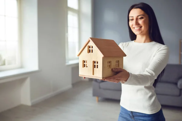 Pareja feliz sosteniendo una maqueta de una casa en sus manos mientras están de pie en una habitación en casa. —  Fotos de Stock