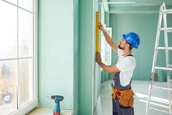 A builder standing on a ladder installs drywall at a construction site — ストック写真