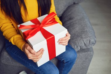 Kırmızı kurdeleli, hediye kutulu mutlu kız odada oturuyor..