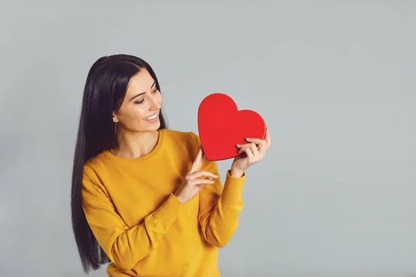 Beautiful girl holding a red heart in her hands on gray background Valentines day. — Stock Photo, Image