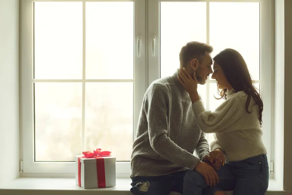 Rear view of a young couple sitting on a window sill by the window looking out the window. Valentines day. — 스톡 사진