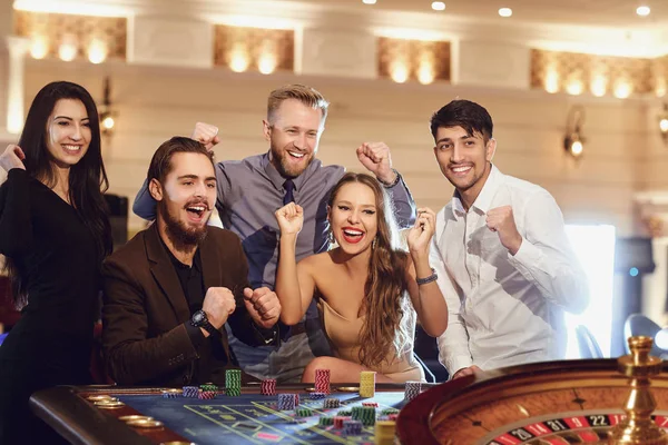 Vrolijke groep vrienden geniet van het winnen van poker roulette in een casino. — Stockfoto