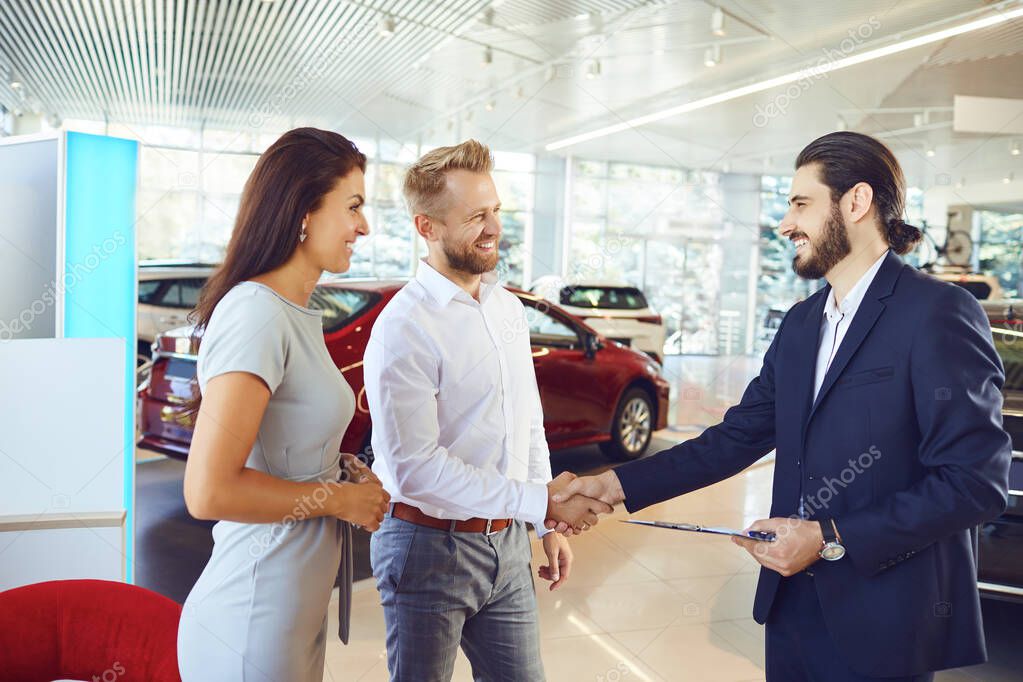 A couple buys a new car. A man and a car salesman make a handshake