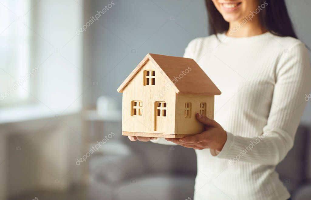 Happy couple holding a mock up of a house in their hands while standing in a room at home.