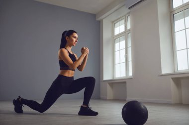 Çömelme egzersizleri. Elinde dambıllarla bir odada çömelme yapan siyah spor giysili bir kız..